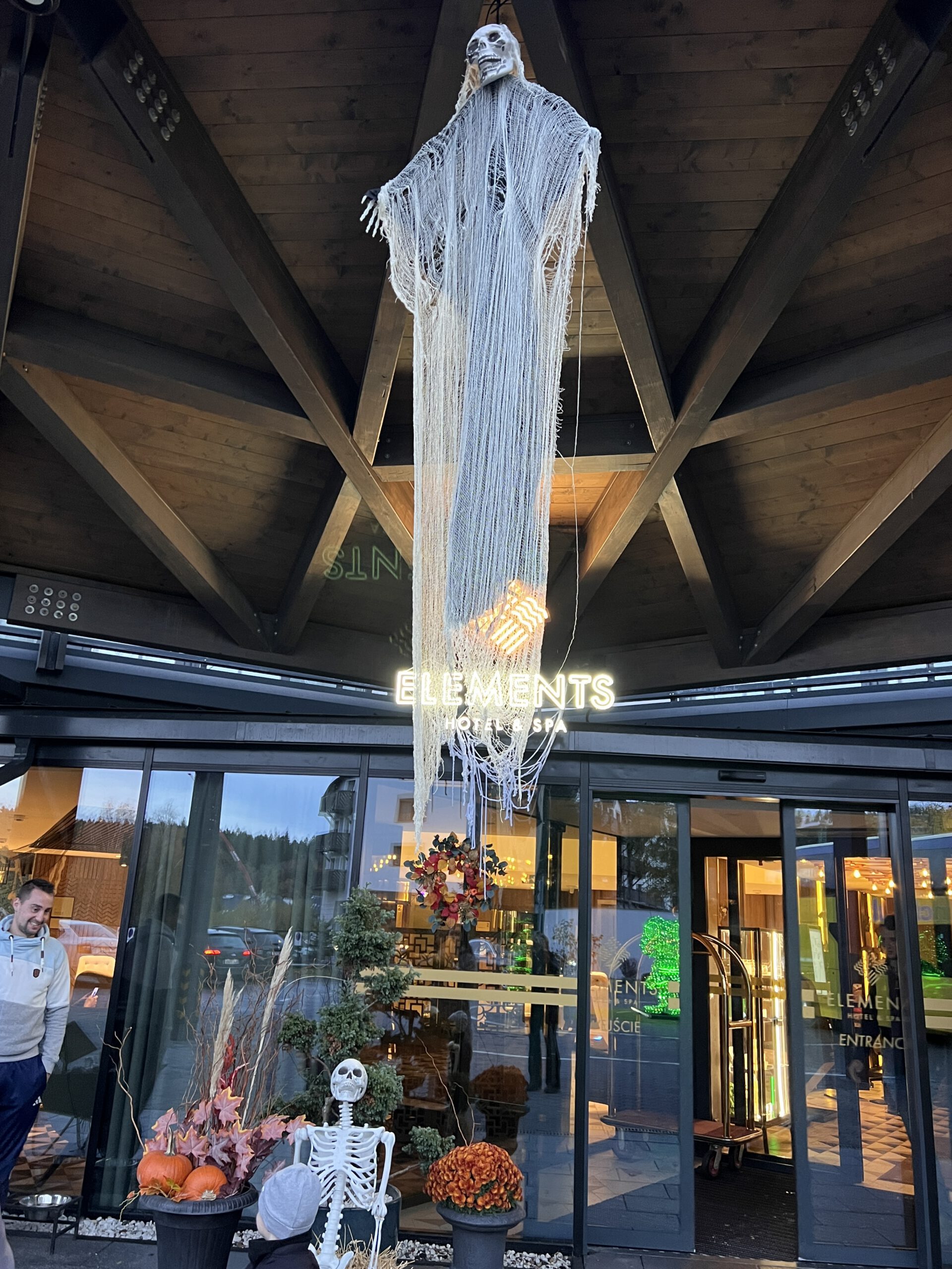 Happy Halloween A hanging ghost decoration and a skeleton greet guests at the entrance of a hotel adorned with autumn decor.